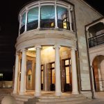 Grand two-story building with columns and curved glass windows photographed at night