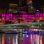 Brisbane Treasury Casino illuminated in pink at night with city skyline and river reflections