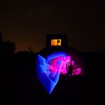 Long exposure light painting with vivid pink and blue trails in front of a WWII radar bunker at night