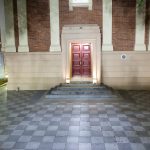 Front entrance of a brick and sandstone building with symmetrical lighting and patterned tiled pathway at night