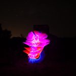 Vertical light painting with vivid pink and blue flame-like trails in front of a WWII radar bunker silhouette at night