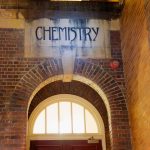 Arched doorway of a heritage brick chemistry building with signage and soft night lighting