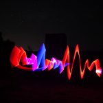 Neon waveform-style light painting in front of a WWII radar bunker at night using red, pink, and blue trails
