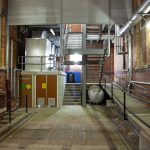 Industrial service corridor with brick walls, exposed pipes, and metal stairs inside a heritage building