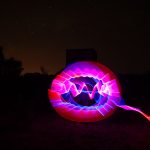 Spherical pink and purple light painting with trailing red beam in front of a WWII radar bunker at night