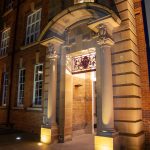 Grand entrance of a brick institutional building with columns and arched portico illuminated at night
