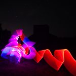 Dynamic light painting with swirling pink and violet light and bold red ribbon in front of a WWII radar bunker at night