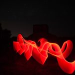 Red light trail forming wave and hook shapes in front of a WWII radar bunker at night
