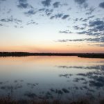 Tranquil lake at sunset with vivid sky reflections, serene horizon, and soft scattered clouds