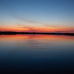 Minimalist lake at dusk with fading orange and blue tones reflecting across calm water
